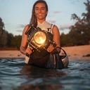 Surf photographer Christa Funk in the sunlight at the beach, holding her big underwater camera